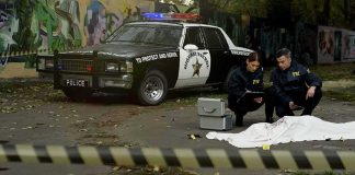 FBI agents examine a covered body at a taped-off crime scene
