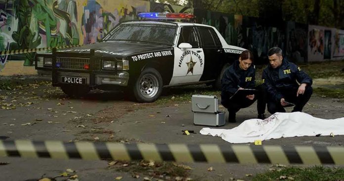 shutterstock_1709493973 FBI agents examine a covered body at a taped-off crime scene