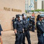 Police officers in riot gear stand in formation outside a headquarters building