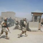 Soldiers in desert uniforms run past a checkpoint amid dust