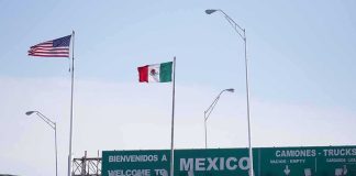 Urgent Mexicali Threat Freezes U.S. Ops Border crossing with U.S. and Mexico flags and a sign welcoming to Mexico