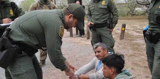 Detained 28 Hours Inside Airport Limbo law enforcement officer handcuffing two seated men outdoors