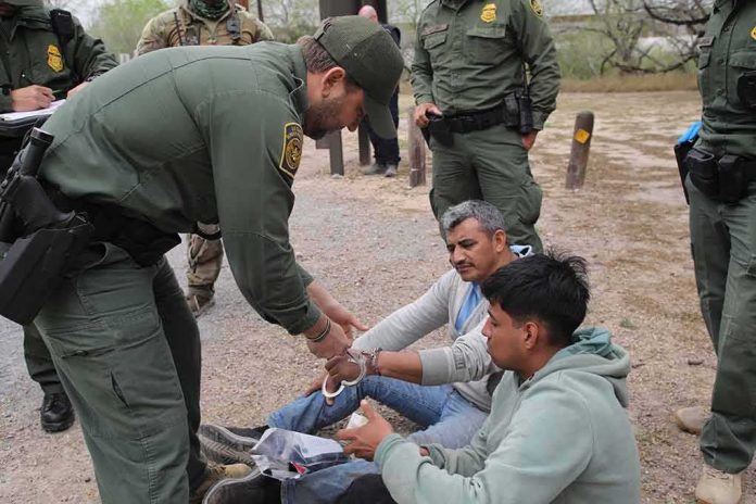law enforcement officer handcuffing two seated men outdoors