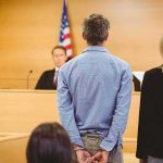 Courthouse Deal Upends Murder Case Defendant in handcuffs stands before a judge in a courtroom