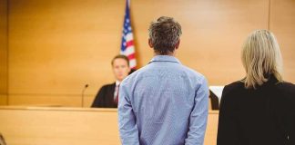 Defendant in handcuffs stands before a judge in a courtroom