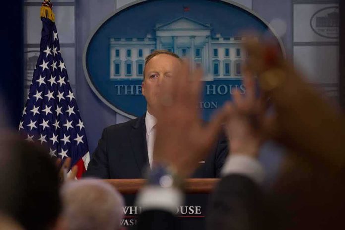 Press secretary at podium with raised hands in briefing room