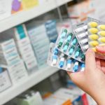 Hands holding blister packs of assorted pills in a pharmacy