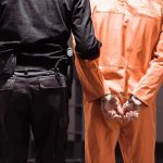 FBI Most Wanted Snared In Somalia Prisoner in orange jumpsuit handcuffed with guard standing beside