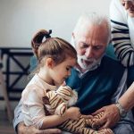 Little girl holding a stuffed tiger with two older adults nearby