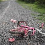 THC Gummies Used On Children? Pink children's bicycle with training wheels lying on a gravel path