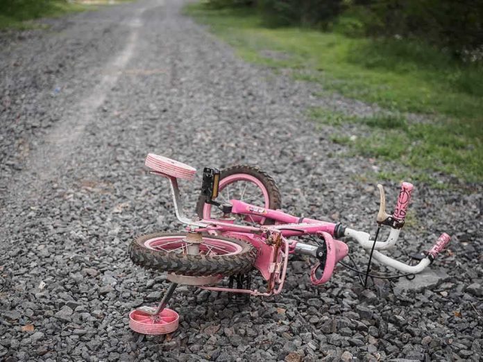 shutterstock_1098020126 Pink children's bicycle with training wheels lying on a gravel path