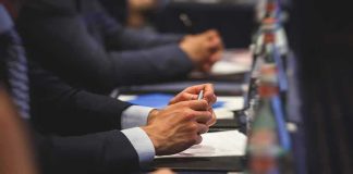 Hands of people in suits taking notes at a conference table