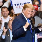 Bribe Or Bonus? Trump’s $5,000 Tease man in suit raising fists at a rally podium