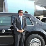 DHS Chief’s Jet Loses Engine Mid-Flight security agent in suit standing beside black limousine near aircraft