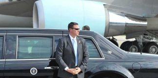 security agent in suit standing beside black limousine near aircraft