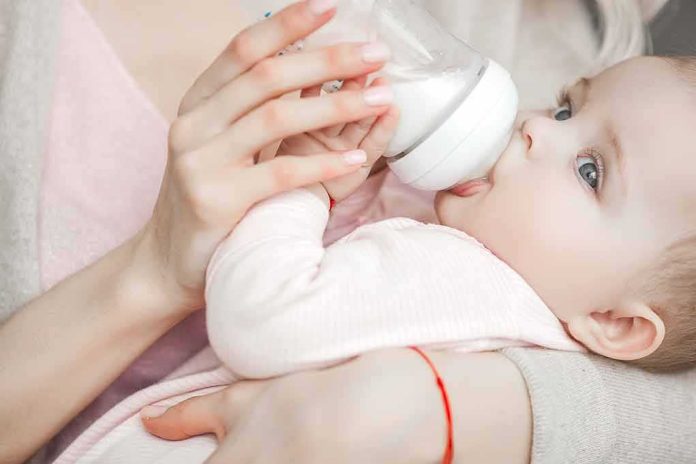 shutterstock_1300509853 Baby drinking from a bottle while being held