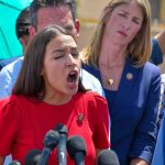 woman in red speaking passionately at microphones