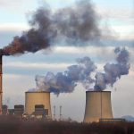Industrial power plant with smokestack and cooling towers emitting smoke
