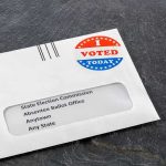 Absentee ballot envelope with I Voted sticker on dark surface