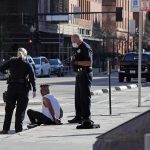 Police officers detain a seated man on a city sidewalk