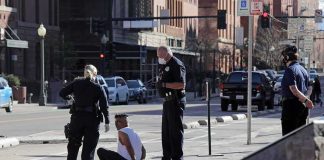 Showdown Over Sanctuary Money Explodes Police officers detain a seated man on a city sidewalk