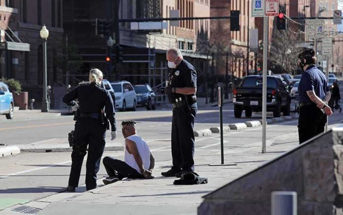shutterstock_1714214569 Police officers detain a seated man on a city sidewalk