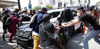 Protesters surround and damage a police vehicle on a city street