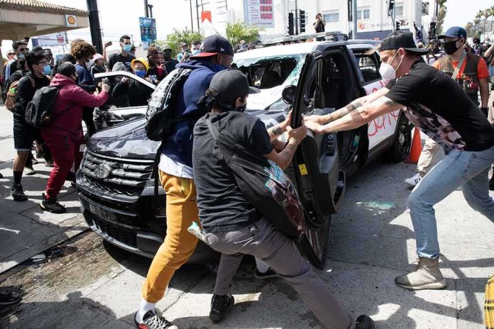 shutterstock_1745191706 Protesters surround and damage a police vehicle on a city street