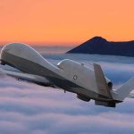 military drone flying above clouds at sunset