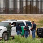 K-9 Sniff Unravels Massive Coke Haul law enforcement officers confer beside patrol vehicles near a border fence