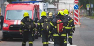 Firefighters walking toward a scene with hoses and a red emergency van