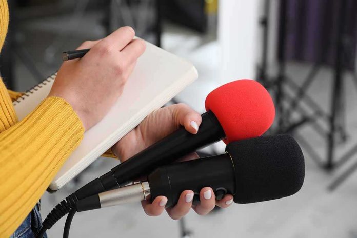 shutterstock_2431198207-1 Journalist holding two microphones while writing in a notebook