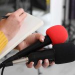 Pentagon Power Play: Base Renamed After Graham Journalist holding two microphones while writing in a notebook