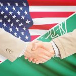 No U.S. Bombs — What’s The Catch? Handshake between two people over U.S. and Saudi flags