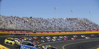 Stock cars racing on a banked track with grandstands in background