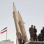 Soldiers stand beside large missiles at an outdoor display