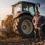 Trump Drops $8B Bomb For Farmers Farmer standing beside a tractor in a plowed field