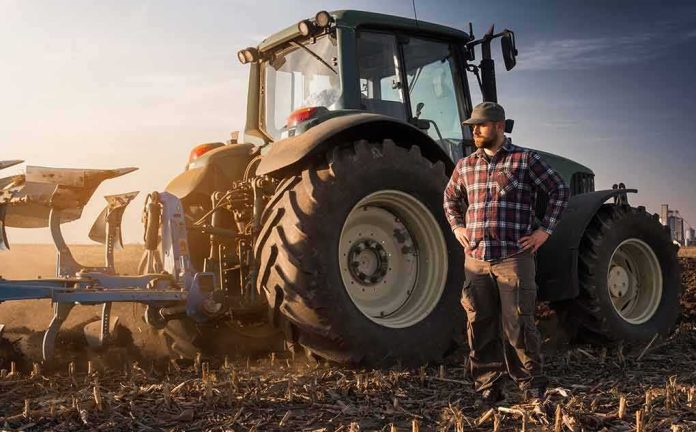 shutterstock_1017616912 Farmer standing beside a tractor in a plowed field