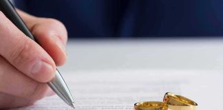 Hand signing a document beside two gold wedding rings