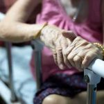 Elderly person’s hands resting on a hospital bed rail