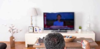 Man watching TV from couch with remote in hand
