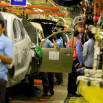Tesla Dust-Up, Triple Homicide Link? Teddy Williams on an automotive assembly line with workers fitting car doors