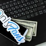 Teacher’s Adult Site Gets Her Fired Smartphone with OnlyFans sticker and cash on a laptop keyboard