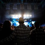 Cowboy-hatted man watches a concert in a packed arena