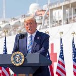 Trump Dangles Billions, Demands Hospital Gatekeepers Fall Donald Trump speaking at a podium with American flags and a ship in the background