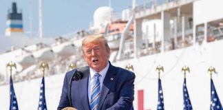 Trump Dangles Billions, Demands Hospital Gatekeepers Fall Donald Trump speaking at a podium with American flags and a ship in the background